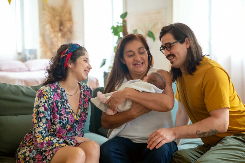 Family gathered close on a couch, leaning in toward a new baby