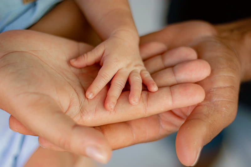 Three generations of hands holding a newborn baby