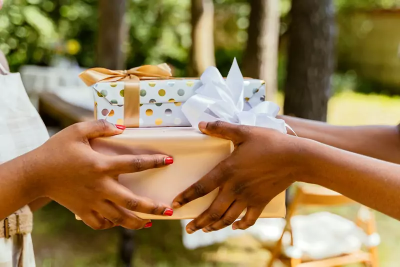 Hands passing wrapped gifts to another pair of hands outdoors