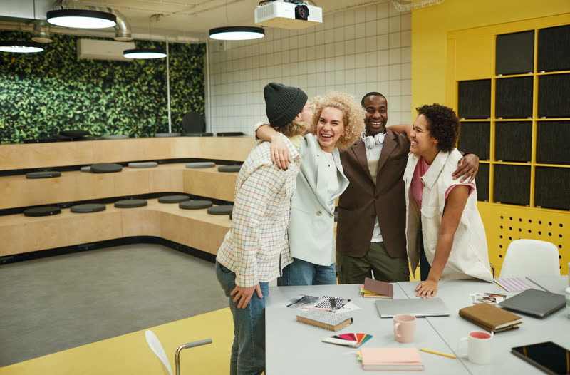 Coworkers gathering for a warm send-off embrace by a desk