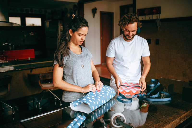 Two people wrapping gifts together at a table