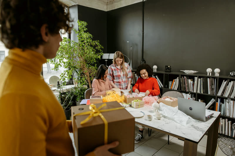 Coworkers preparing wrapped gifts together at a table