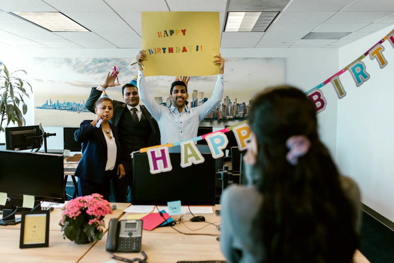 Coworkers surprising a colleague at their desk